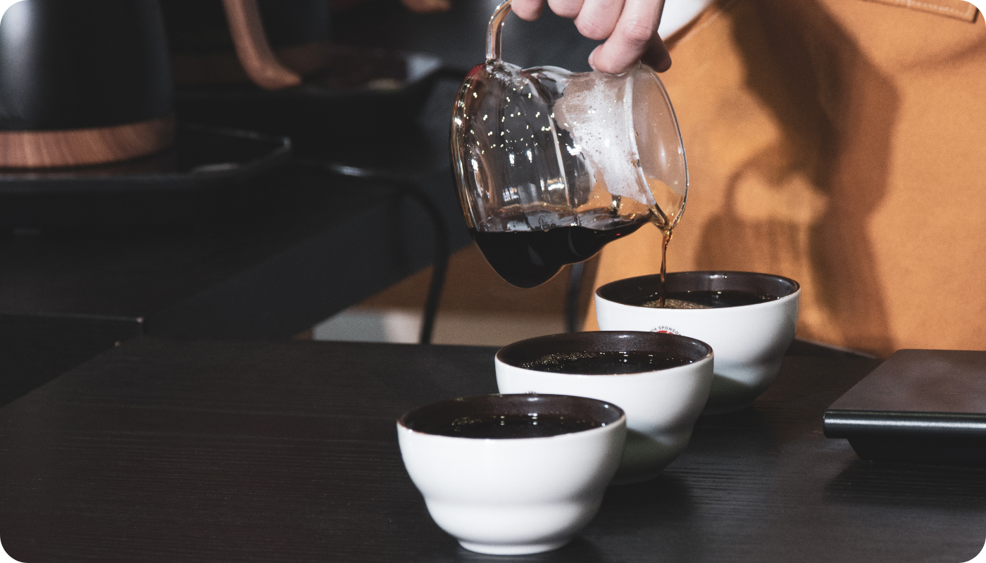 Hand pouring coffee into coffee cups, likely at a coffee tasting event