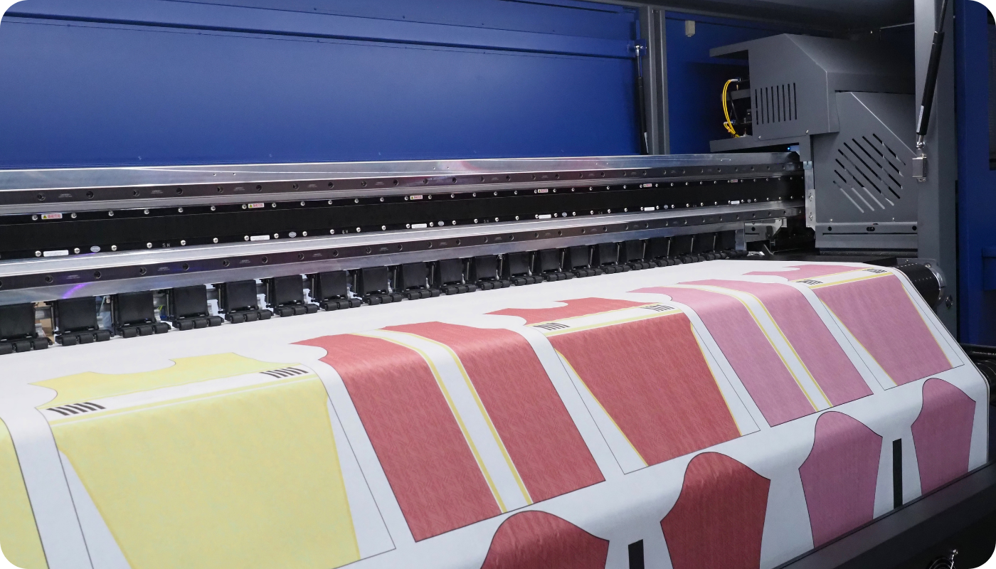 Large-scale sublimation printer printing a roll of t-shirt panels in red and yellow tones, illustrating the process of dye-sublimation used for vibrant, all-over garment prints.