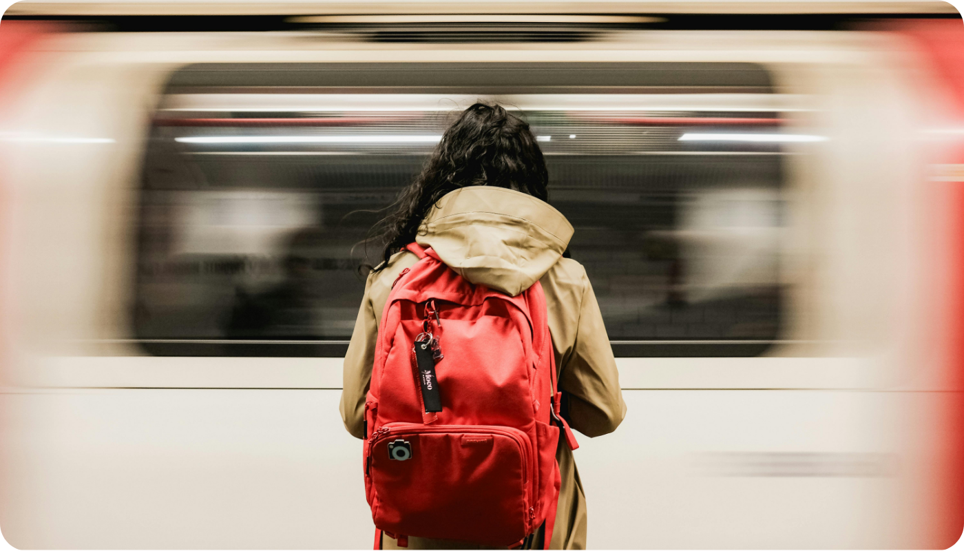Woman with bright red backpack standing in front of moving train