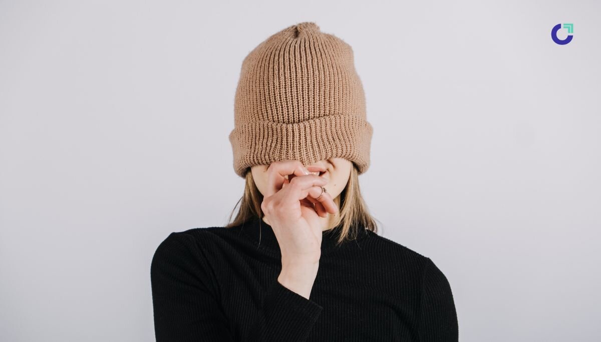 Person in black shirt pulling beige knit beanie over their eyes, symbolizing the struggle of finding the right custom merch ideas.