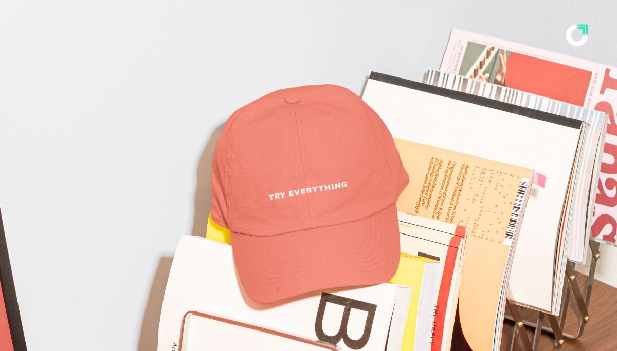 Photo showing a bright peach colored hat on top of a magazine rack. The hat reads 
