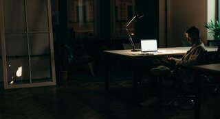 someone sitting in the dark at a desk with their laptop