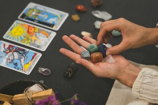 three tarot cards on a table and a hand holding gems