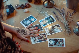 a tattooed hand spreading 6 tarot cards on a table