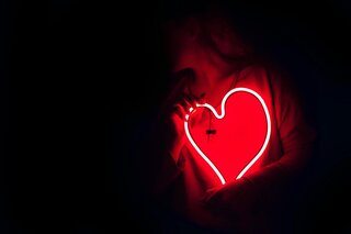 someone in shadow holding a glowing neon heart