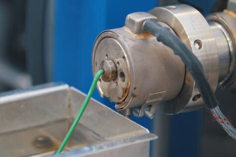 Nahaufnahme einer Extrusionsmaschine, die einen grünen Kunststoffstrang in ein Metallbecken extrudiert