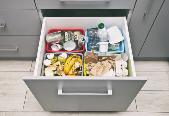 Geöffnete Küchenschublade mit vier Müllbehältern, sortiert nach Papier, Plastik, Dosen und Biomüll
