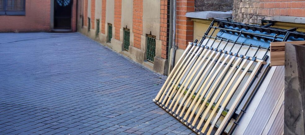 Mehrere Lattenroste und Matratzen lehnen an einer Hauswand auf einem gepflasterten Gehweg