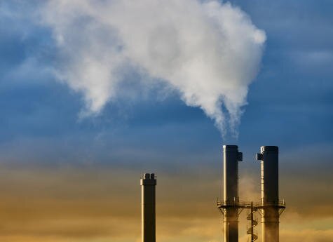 Rauchwolken steigen aus den Schornsteinen eines Industriegebäudes gegen einen blauen Himmel mit Wolken