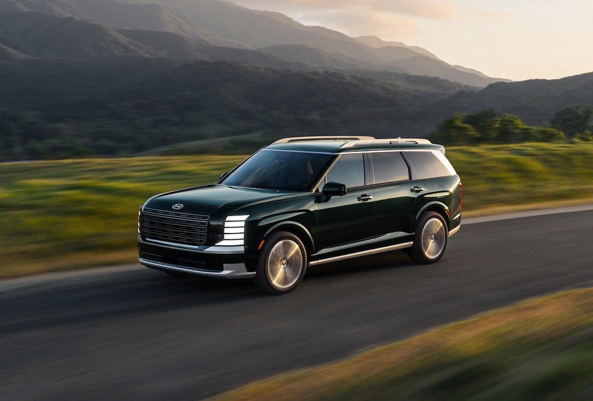 2026 Hyundai PALISADE green front three-quarter driving along a road with mountains in the background