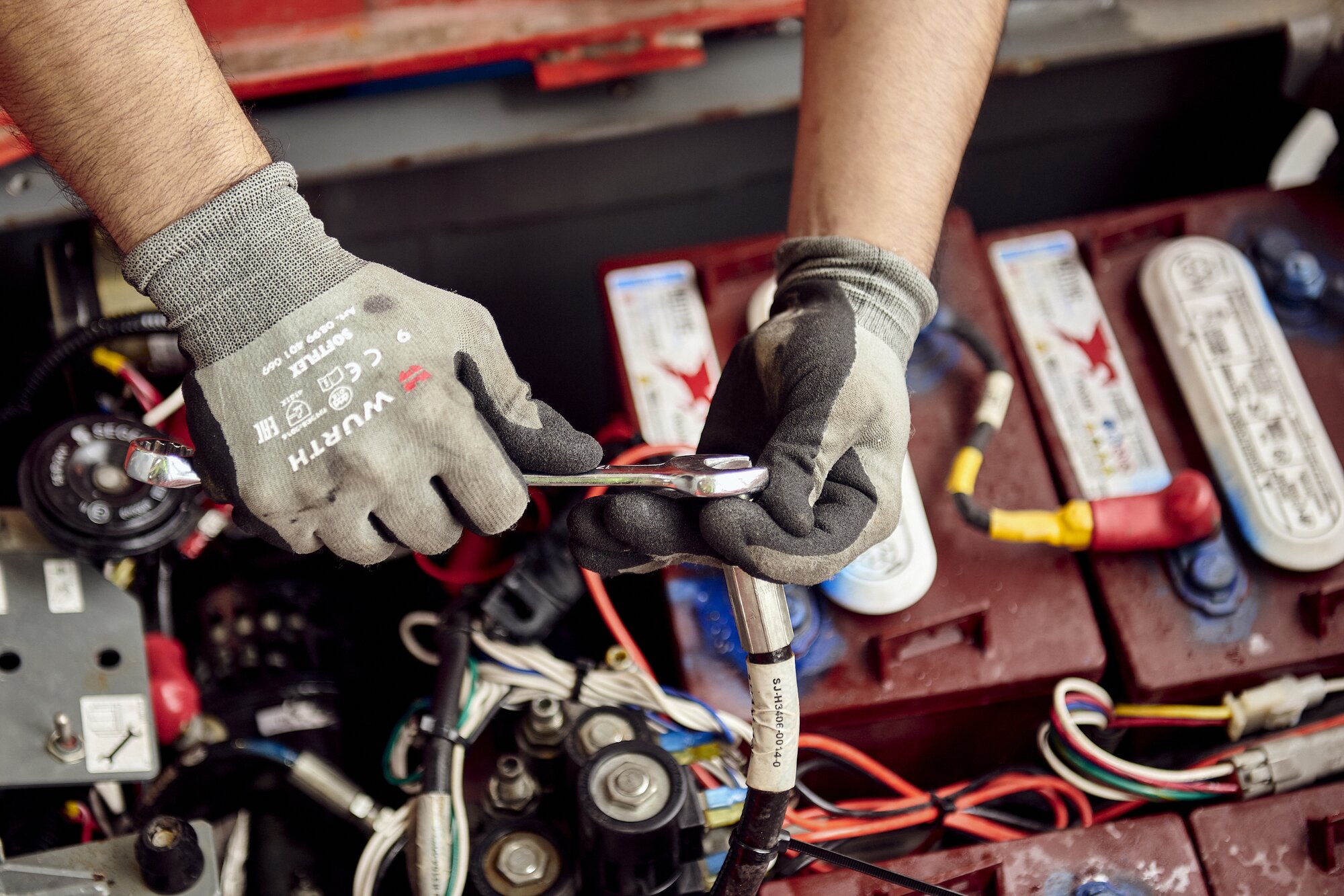Technician performing battery maintenance on access equipment using insulated hand tools.