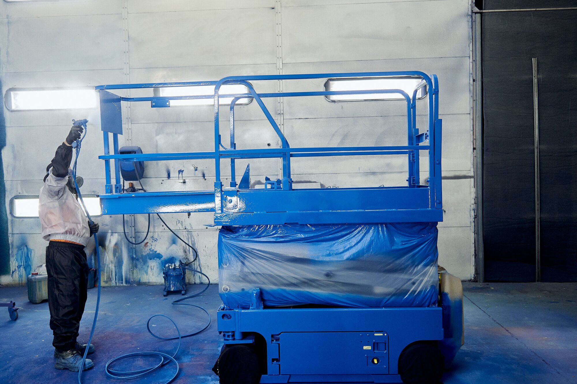 Technician repainting a scissor lift platform during equipment refurbishment.