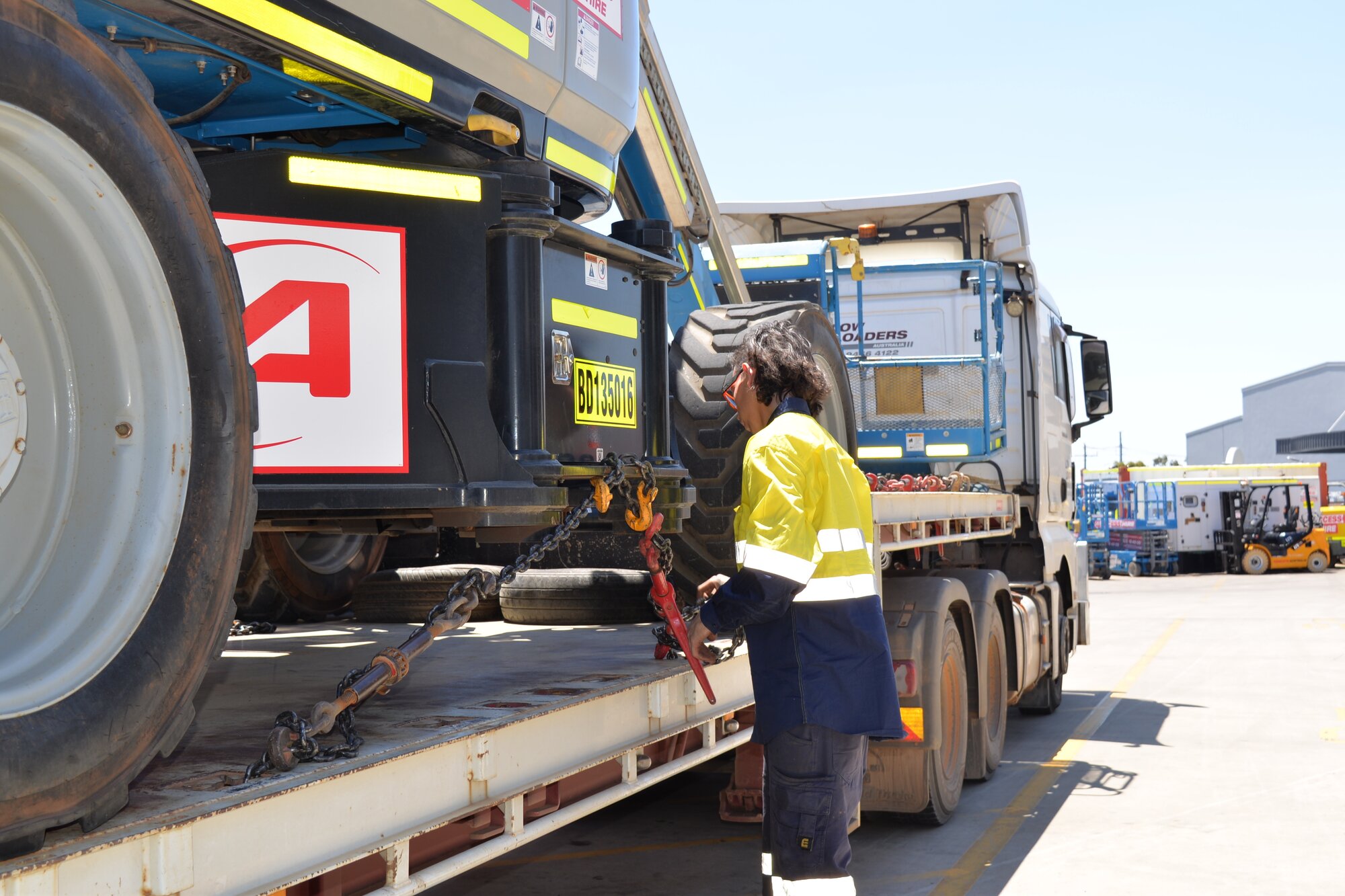 Technician securing a scissor lift onto a transport trailer at Access Hire's Canning Vale facility, Western Australia.