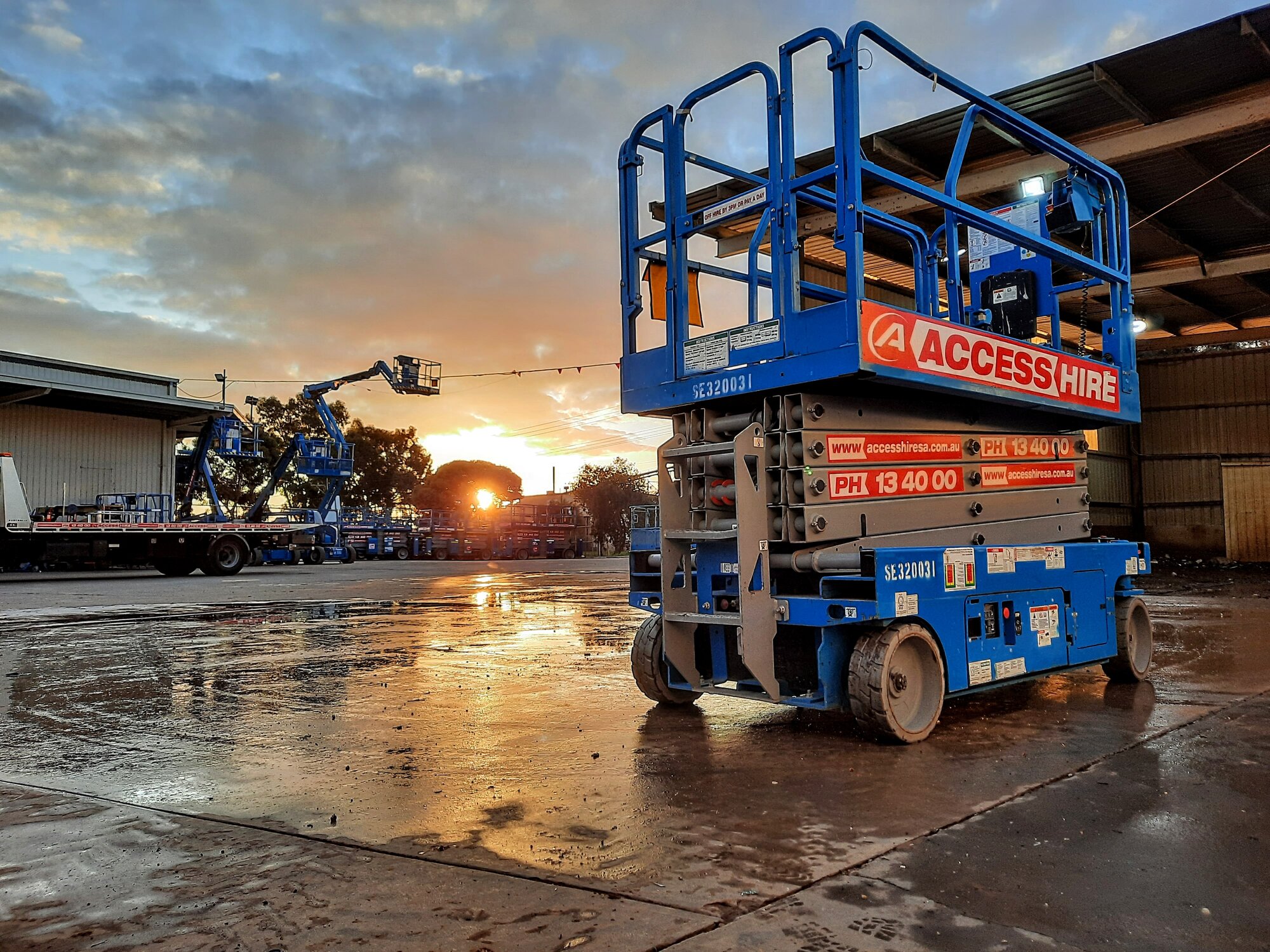 Genie electric scissor lift at the Access Hire wash bay during sunset.
