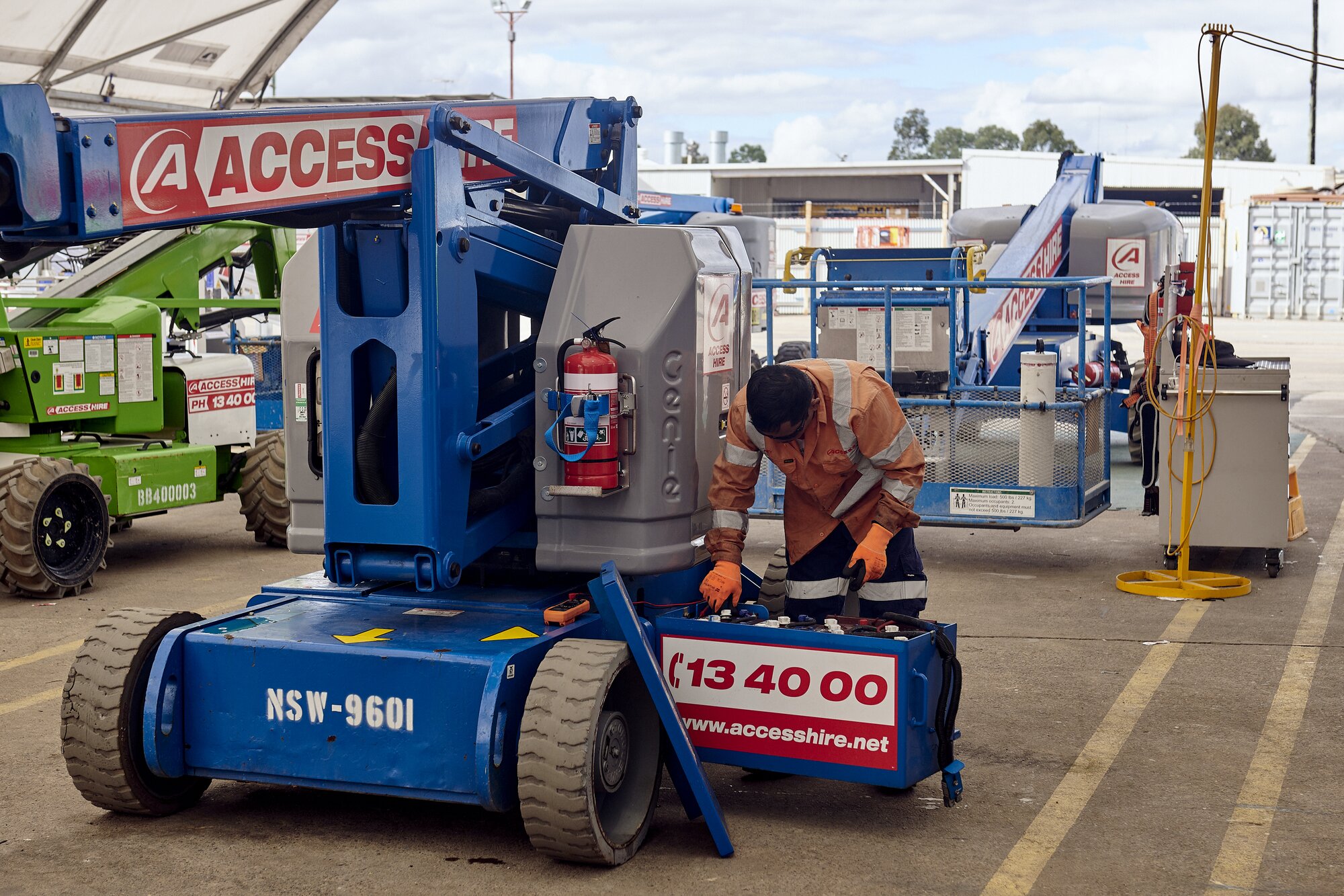 Technician performing maintenance on an articulated boom lift at an Access Hire workshop.