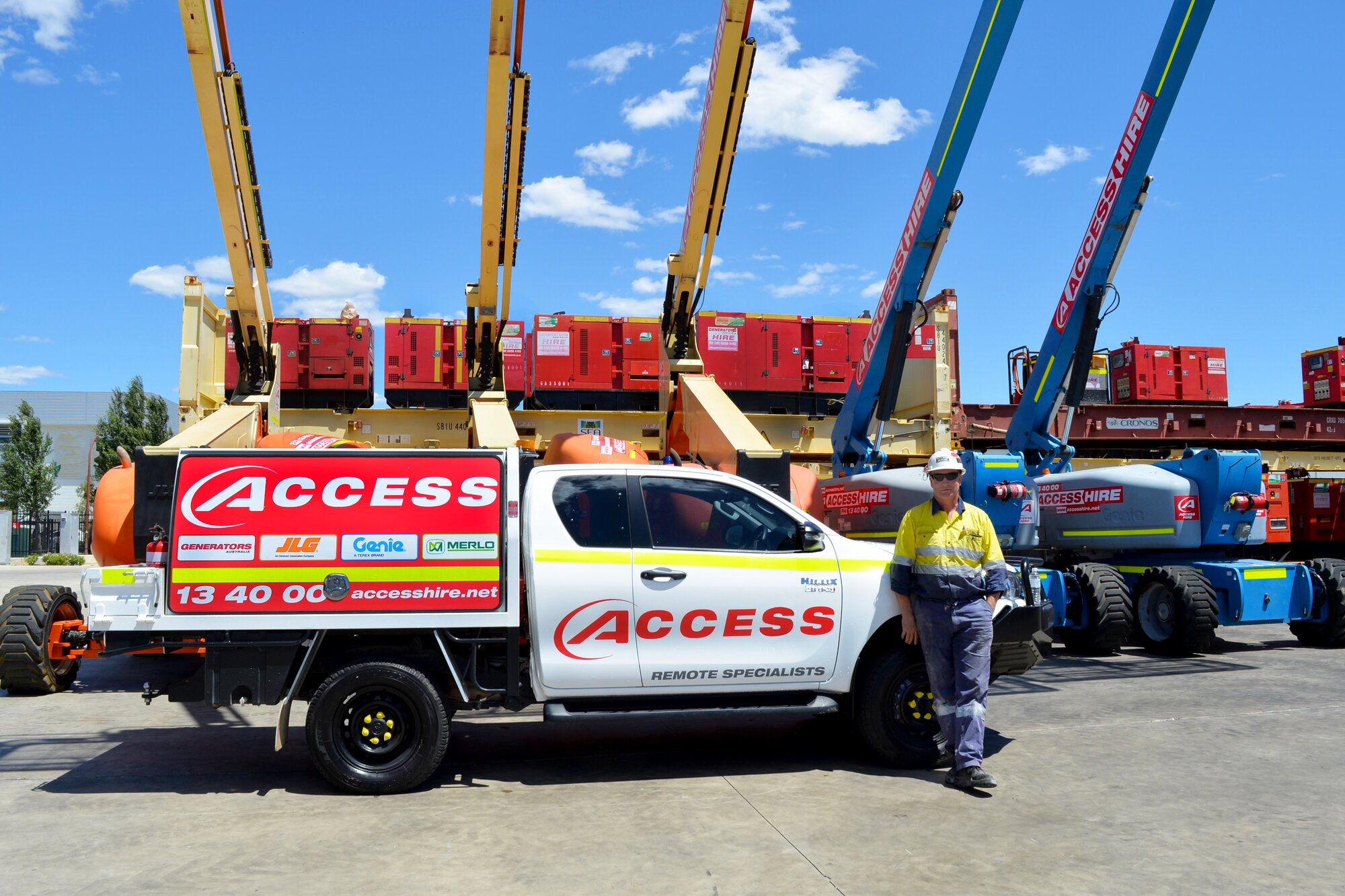 Access Hire remote service specialist standing beside a service vehicle with boom lifts and generators in the equipment yard