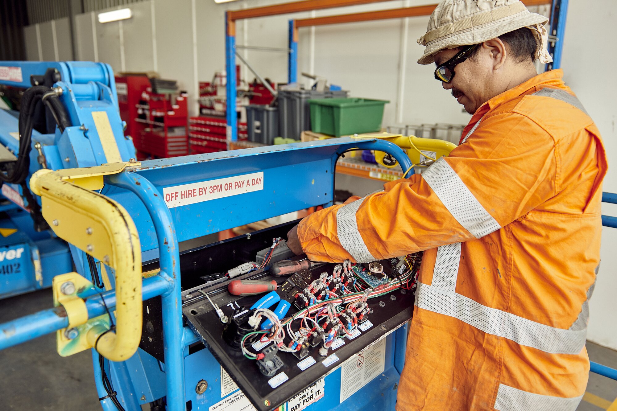 Technician performing maintenance on an Access Hire boom lift in the workshop.