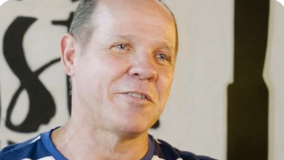 Pedro: Homem de camiseta listrada em frente a uma parede decorada com as palavras pizza e pasta.