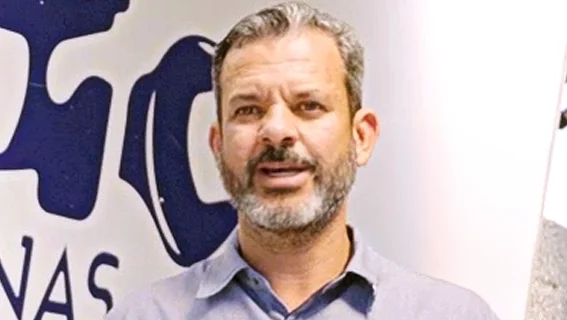 Foto do cliente Alexandre do Centro Auto Sul Minas. Um homem branco vestindo uma camisa social azul clara, falando ao fundo de um outdoor do Centro Auto Sul Minas.