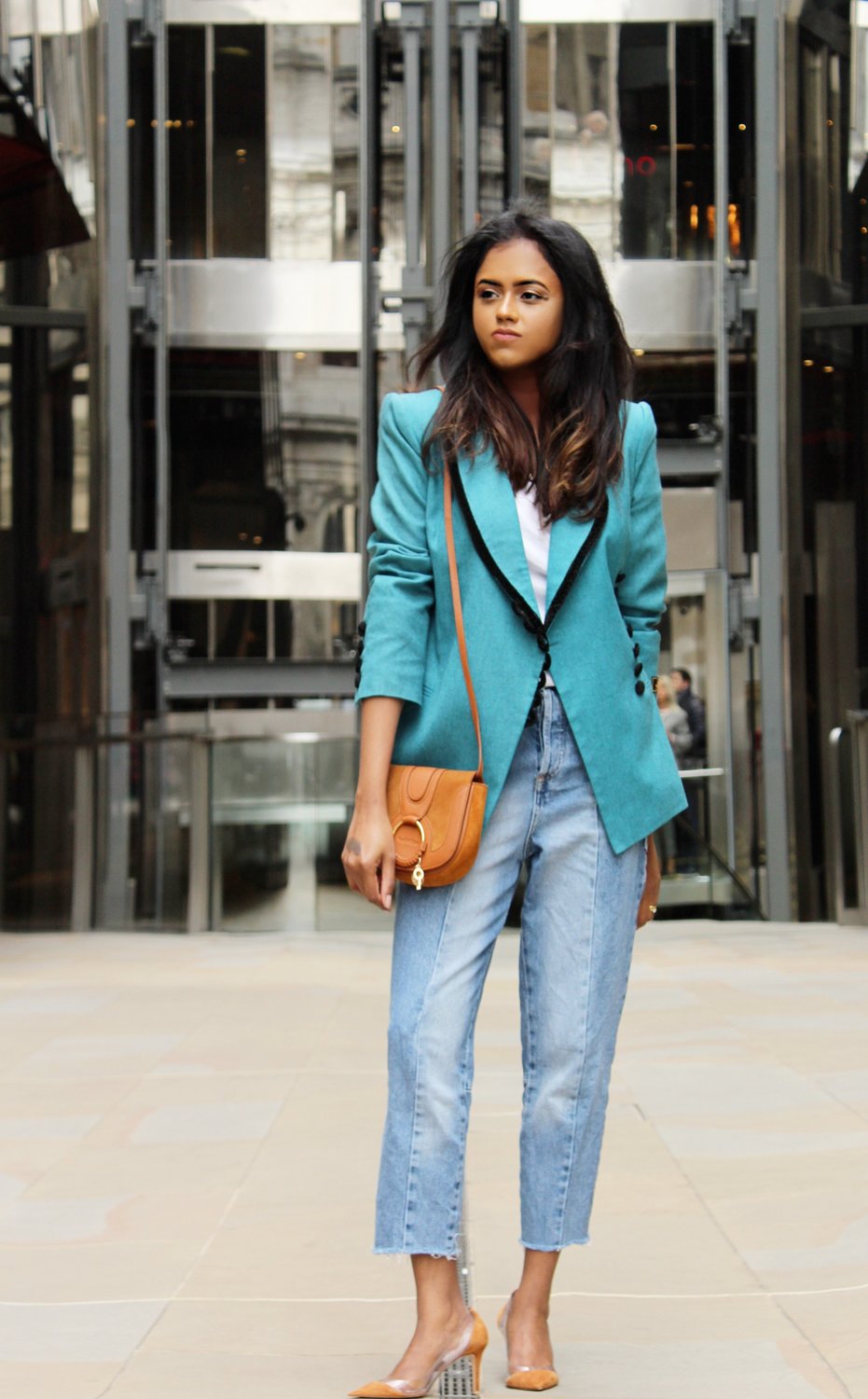 Sachini standing in a shopping street wearing a light blue Fendi vintage blazer, blue jeans and brown Gianvito Rossi heels with a brown handbag