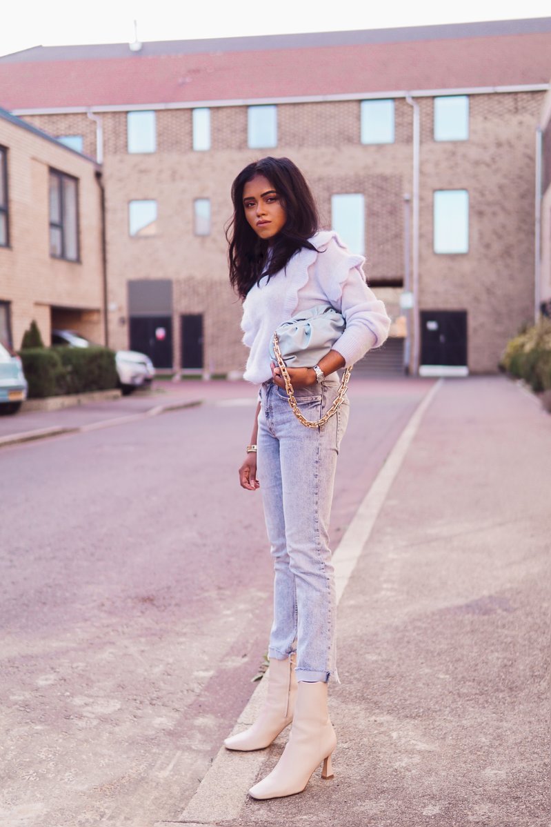 Sachini wearing a light blue top, blue jeans and white boots holding a blue handbag