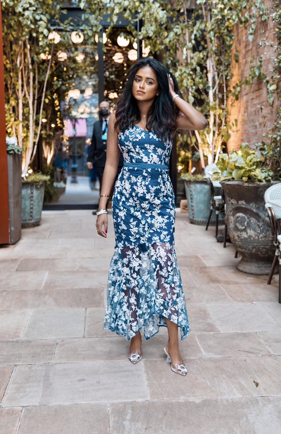 Sachini standing in an alley with trees in the background wearing a blue Chi Chi London dress