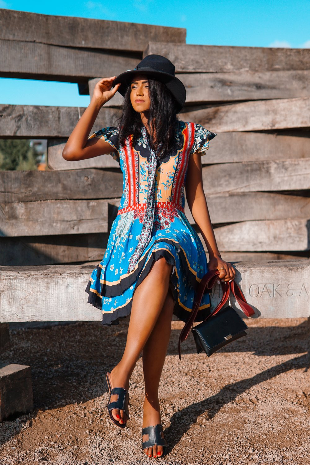 Sachini sitting wearing a Alice and Olivia dress and black hat