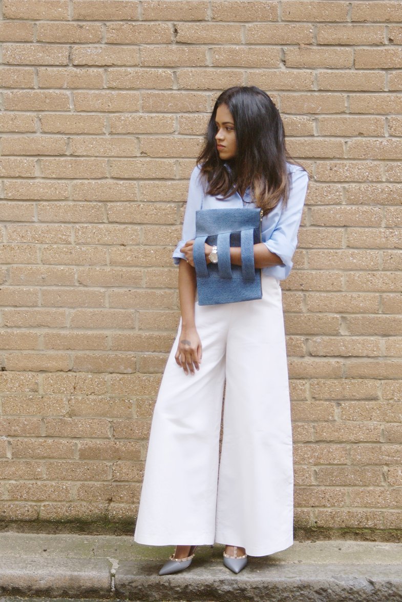 Sachini wearing a blue top, Valentino shoes and white trousers holding a jean colour Embellished Truth bag