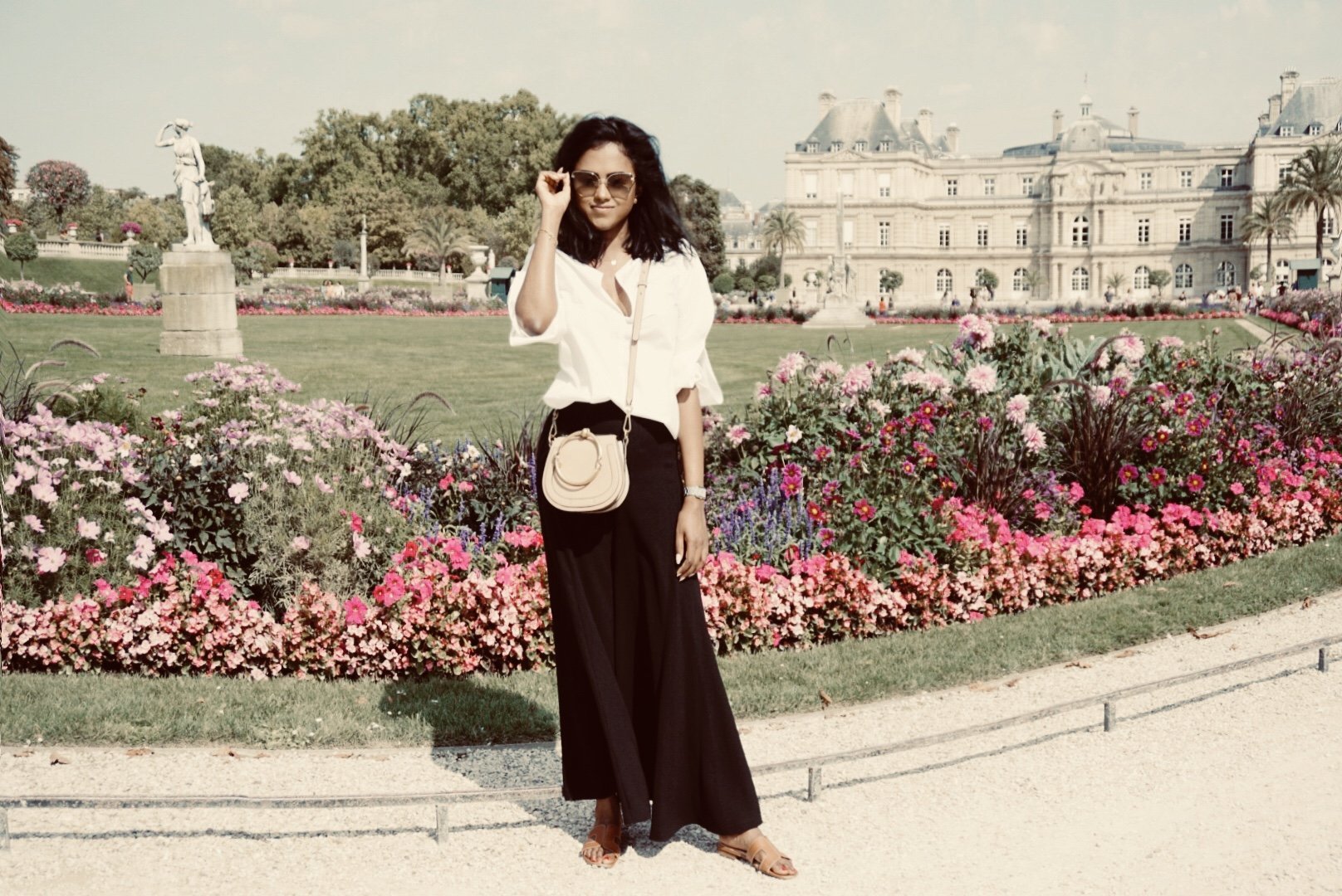 Sachini wearing a white shirt, black trousers, Chanel sunglasses and a Chloé bag in the Jardin du Luxembourg