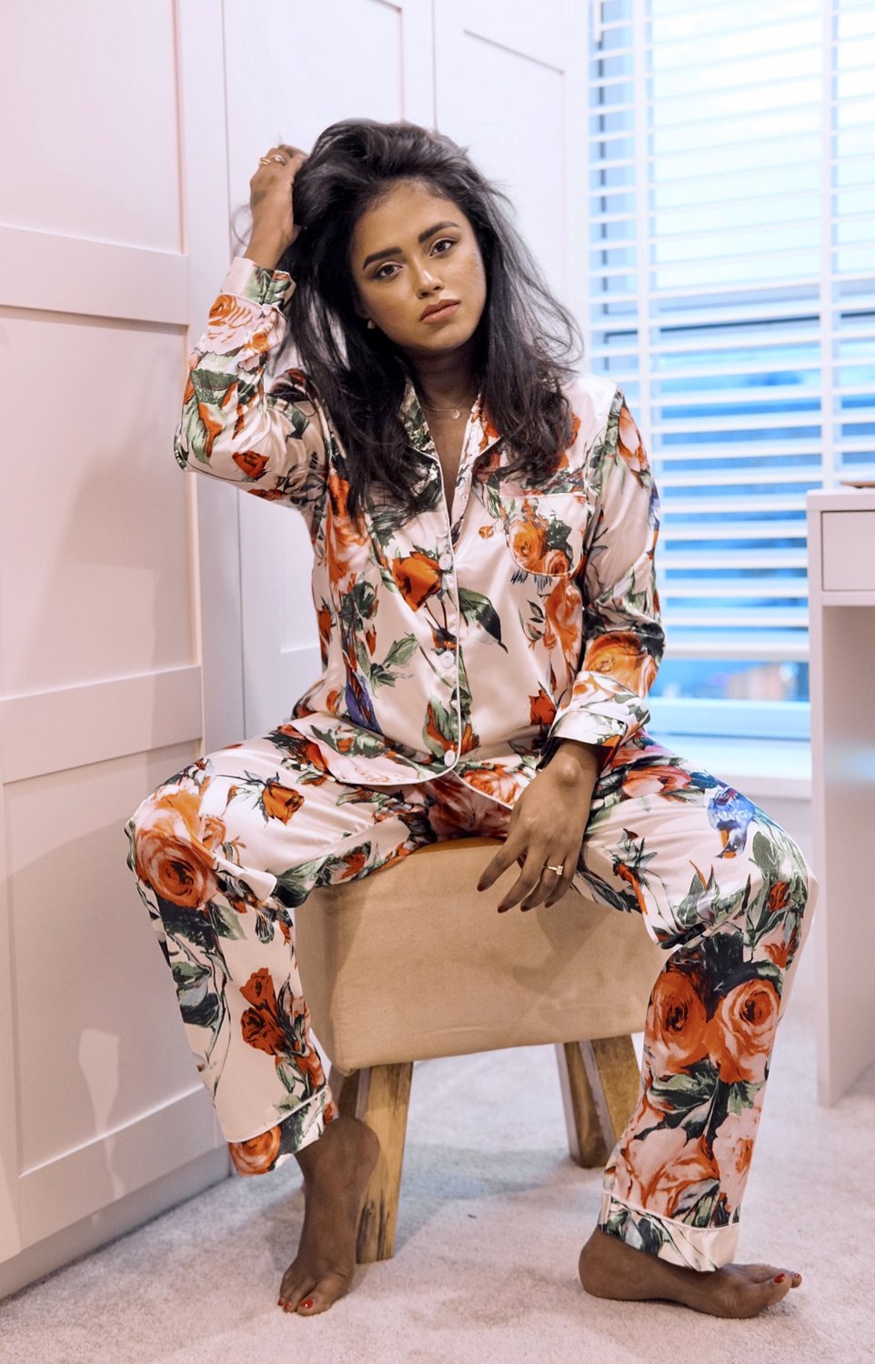 Sachini sitting in front of a wardrobe wearing a white Chi Chi Clothing pyjama set with flowers