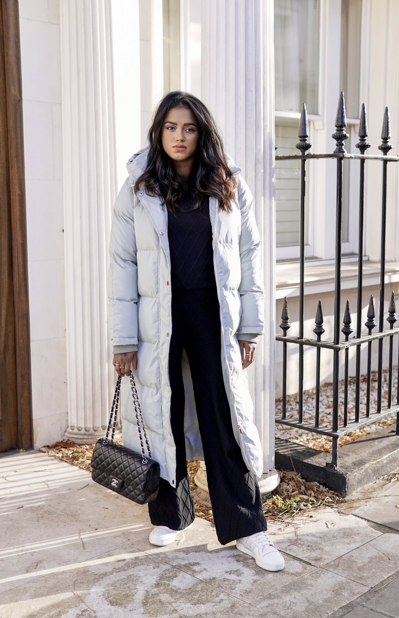 Sachini wearing a light grey Chi Chi London parka and a black Chanel bag in front of white building