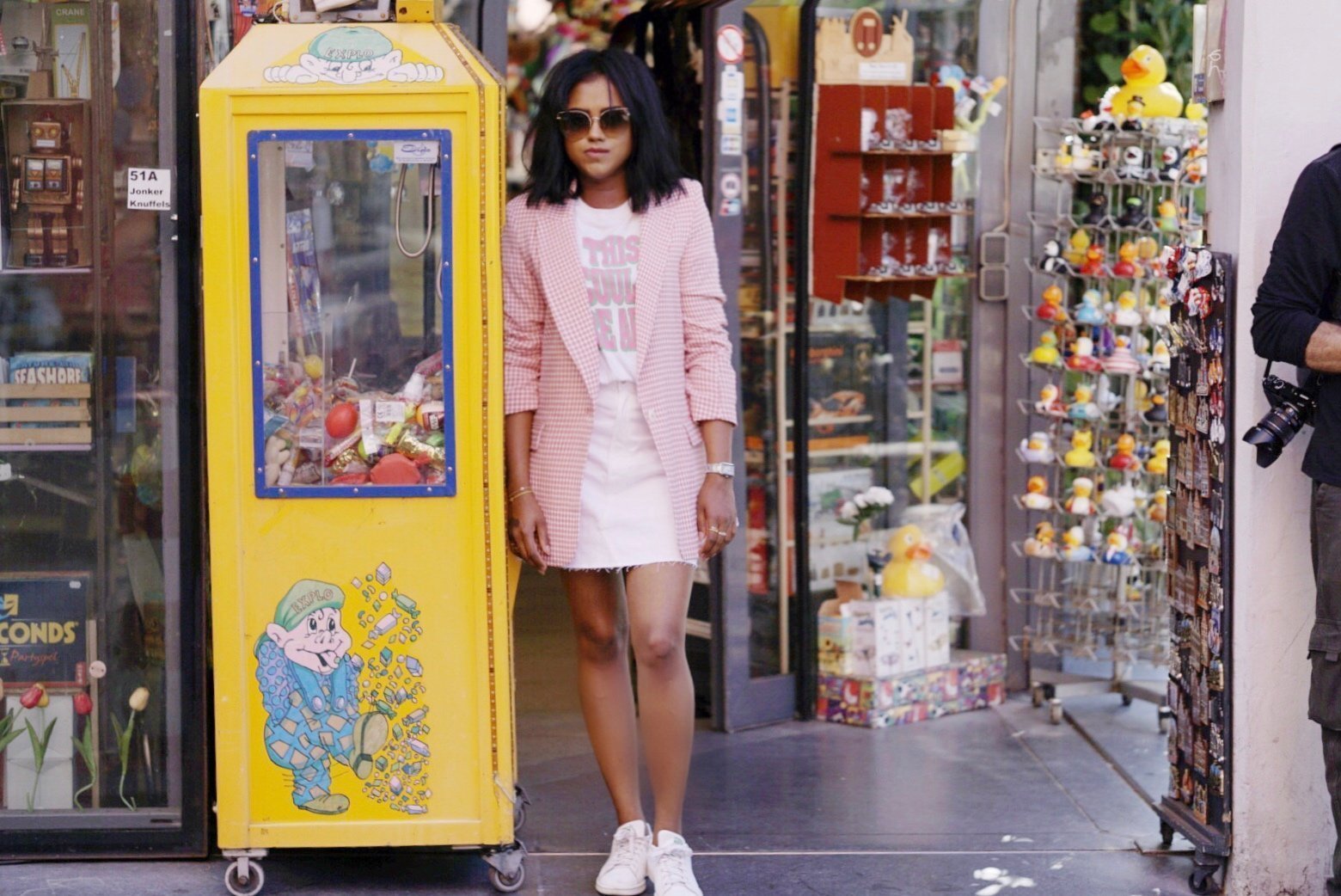 Sachini wearing a pink blazer and a white skirt in front of a shop