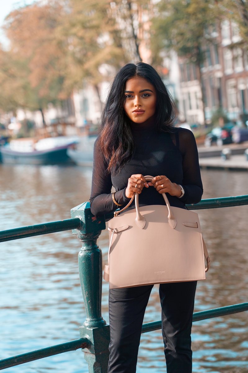 Close up of Sachini standing in front of a canal in Amsterdam wearing a black top and holding a beige Teddy Blake bag
