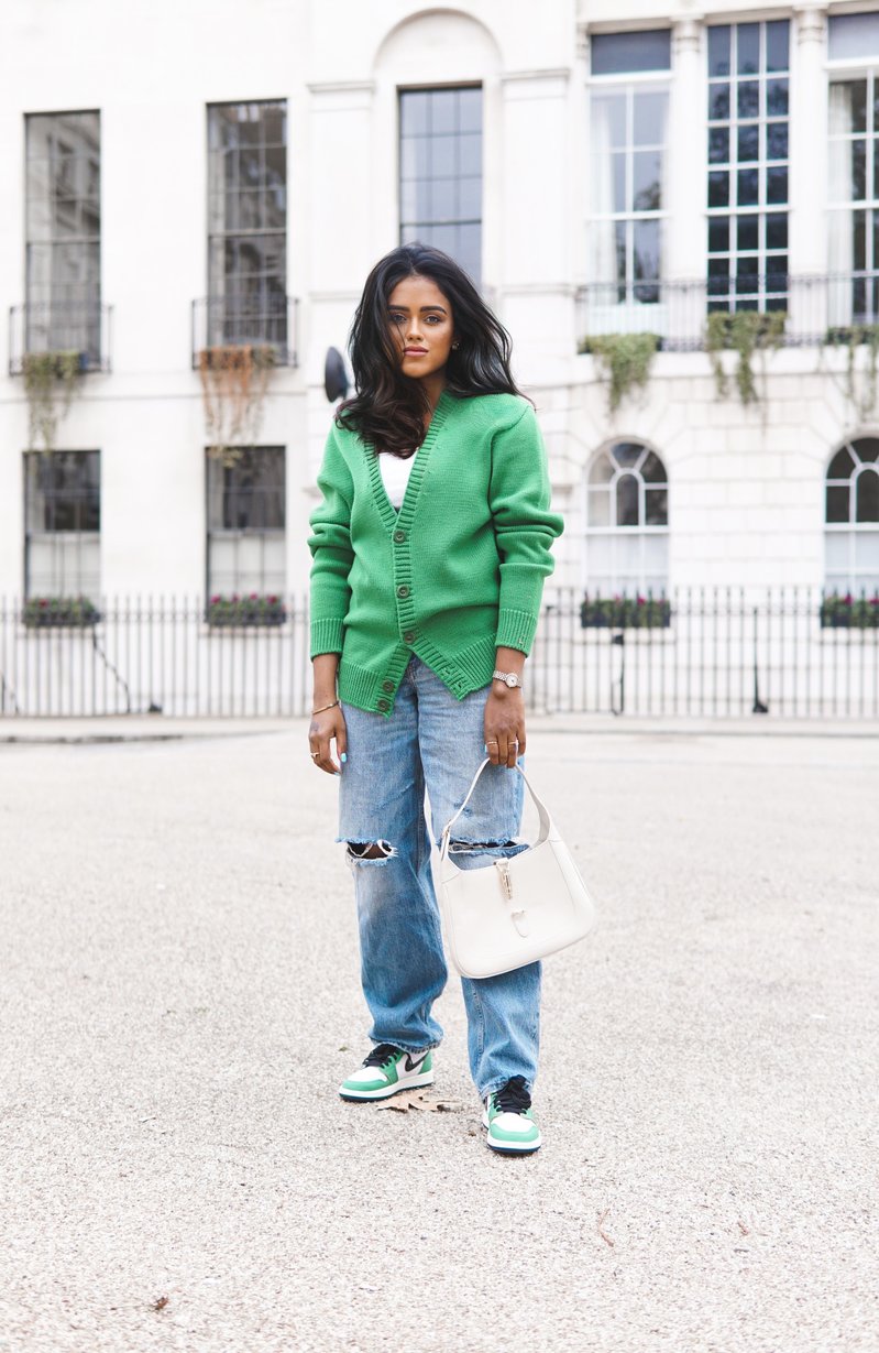 Sachini wearing a green Sheep Inc cardigan, blue ripped jeans and green Nike Air Jordan sneakers holding a white Gucci bag