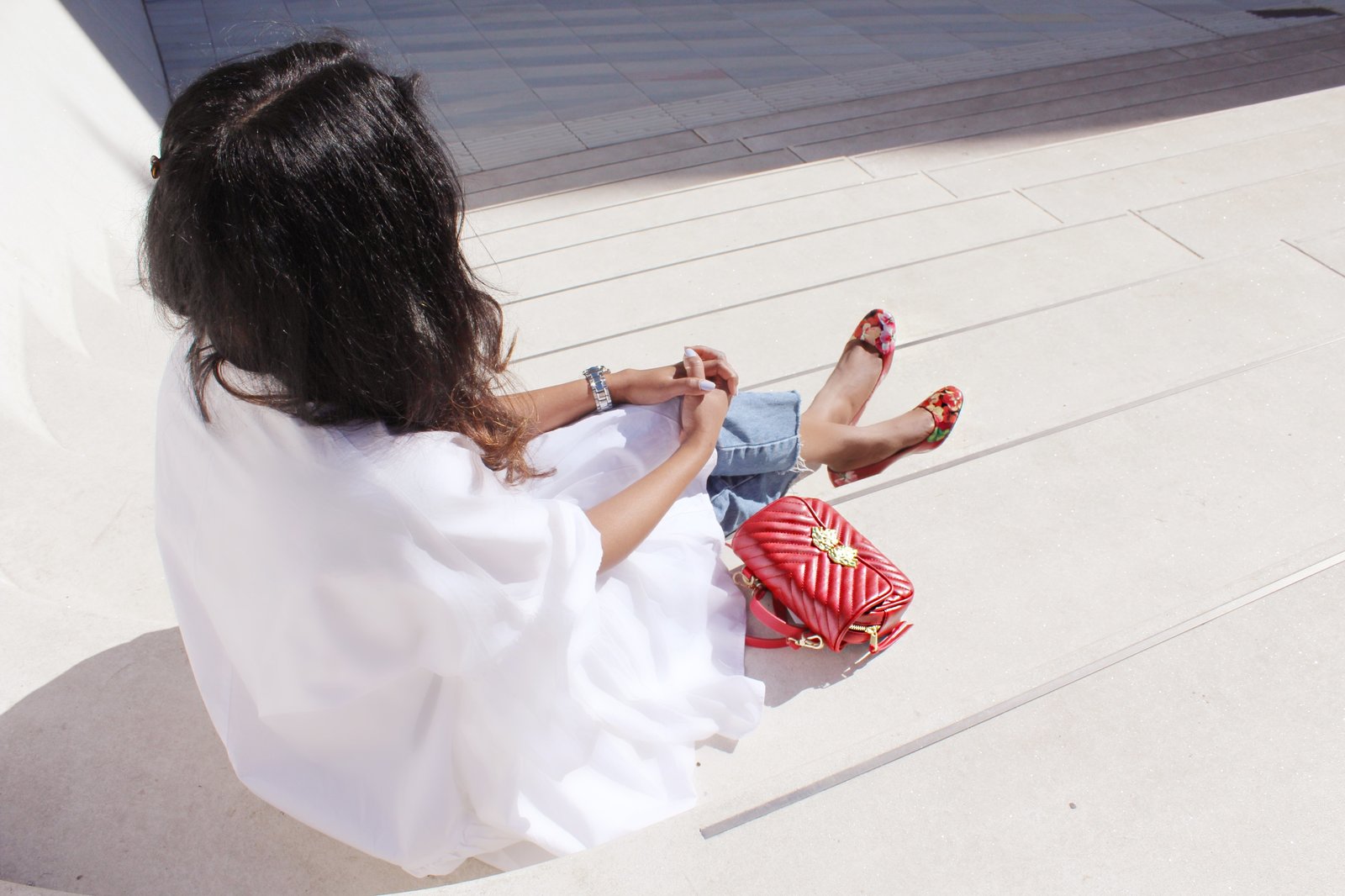 Sachini sitting wearing a white dress, red Gucci shoes and Levi's jeans