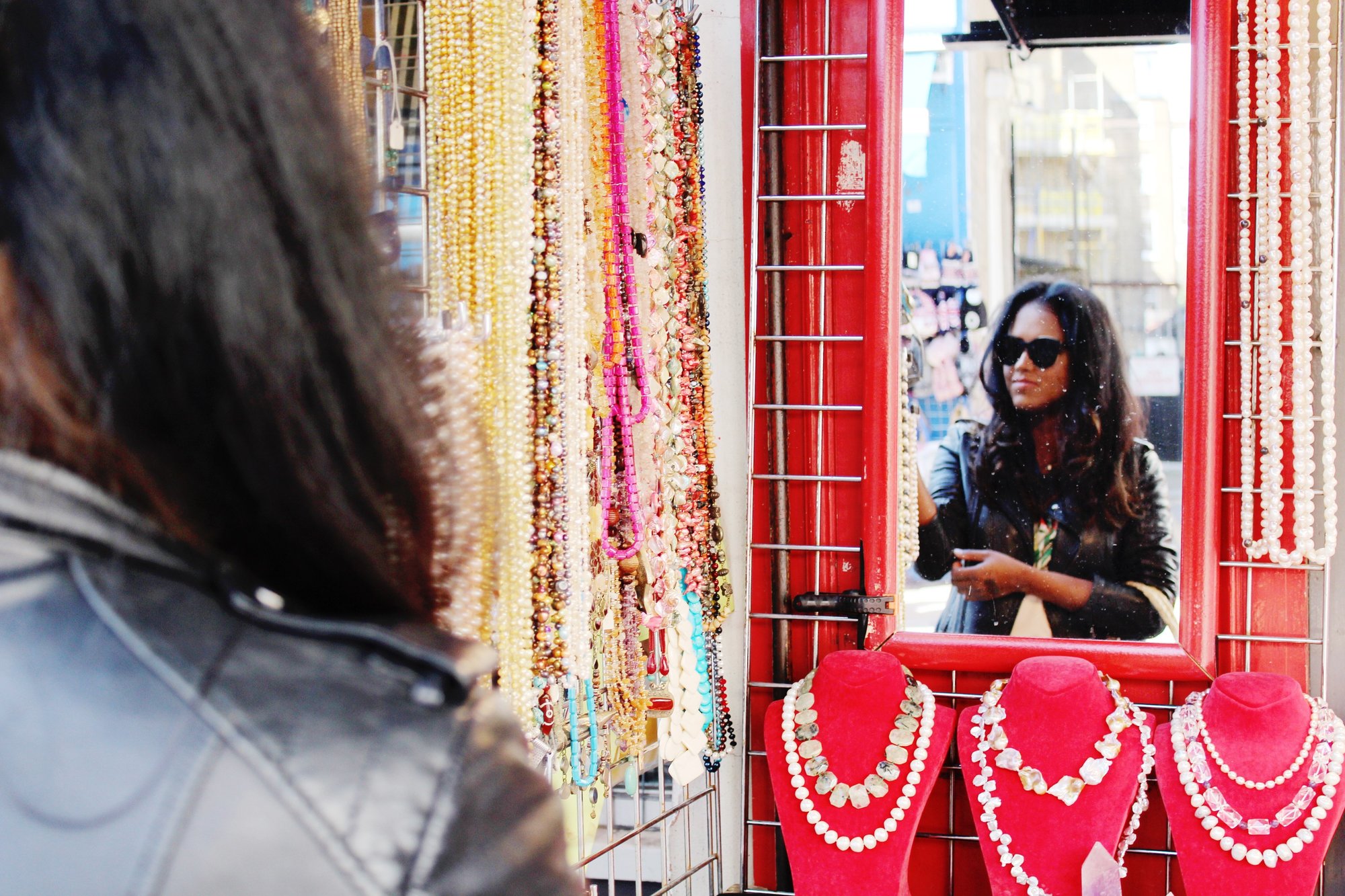 Sachini wearing a black leather jacket looking in a mirror of a street shop