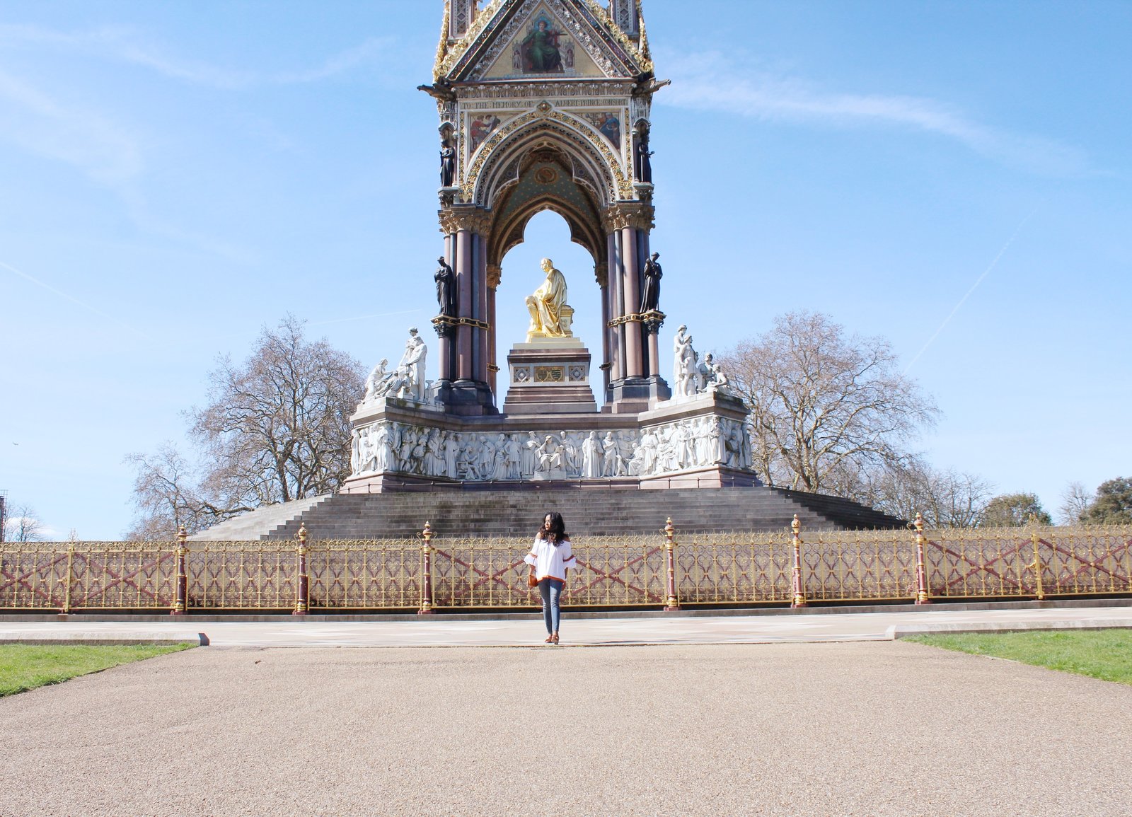 Sachini in front of a statue wearing a white top, blue jeans, brown Gucci shoes with a brown handbag