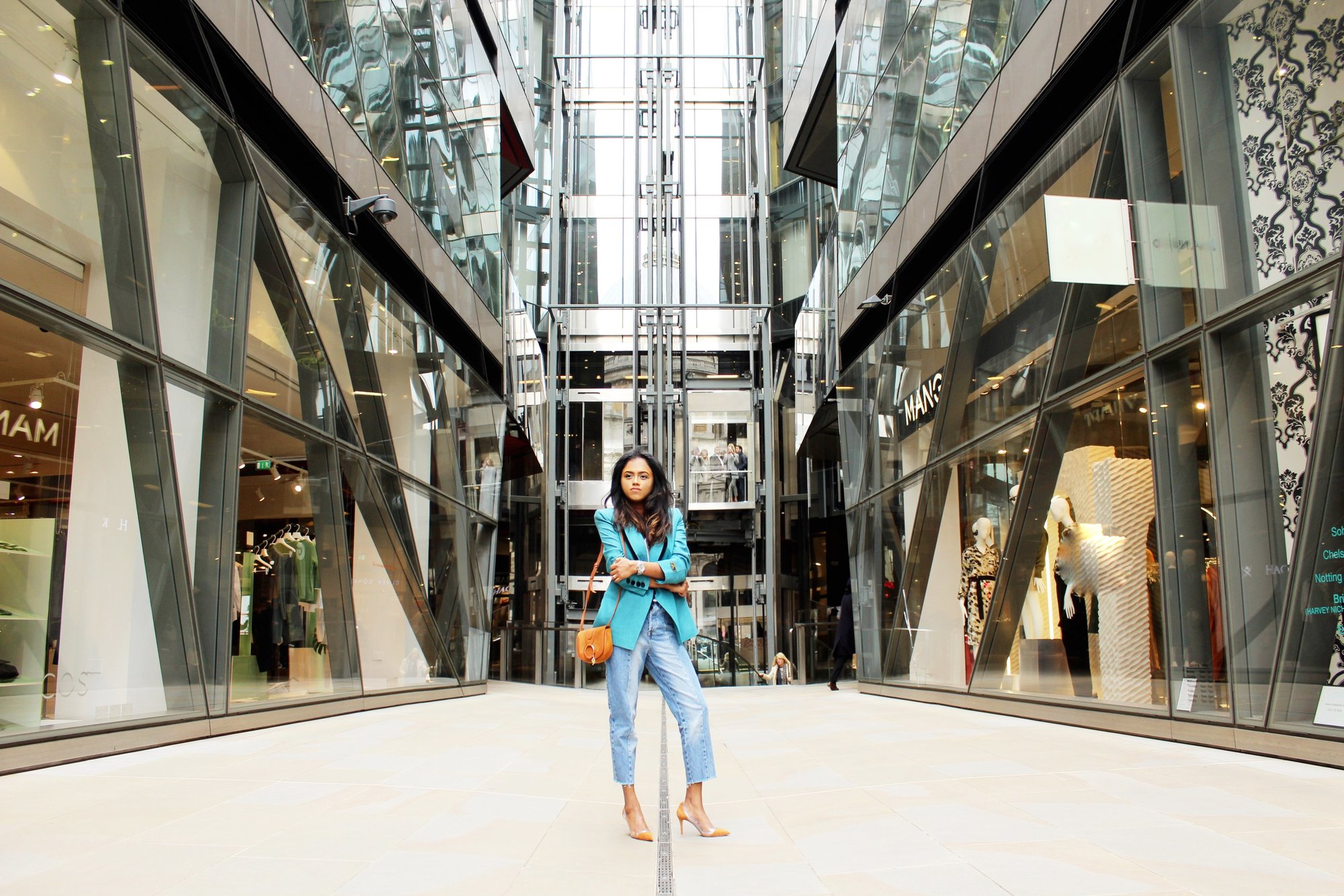 Sachini standing in a shopping street wearing a light blue Fendi vintage blazer, blue jeans and brown Gianvito Rossi heels with a brown handbag