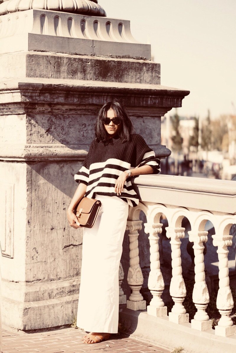 Sachini in Amsterdam on a bridge wearing black and white knitwear, white culottes holding a brown Celine bag