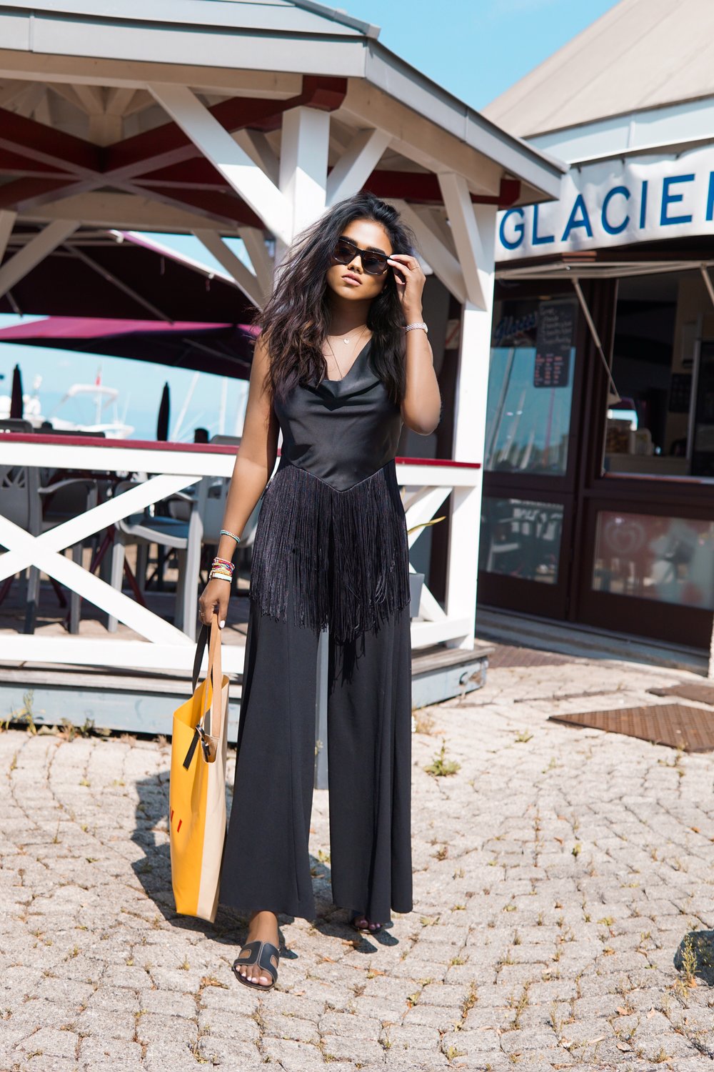 Sachini in front of a cafe wearing a black dresses and sunglasses holding a yellow Marni bag