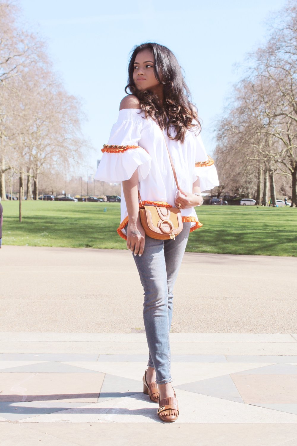 Close up of Sachini wearing a white top, blue jeans with a brown handbag