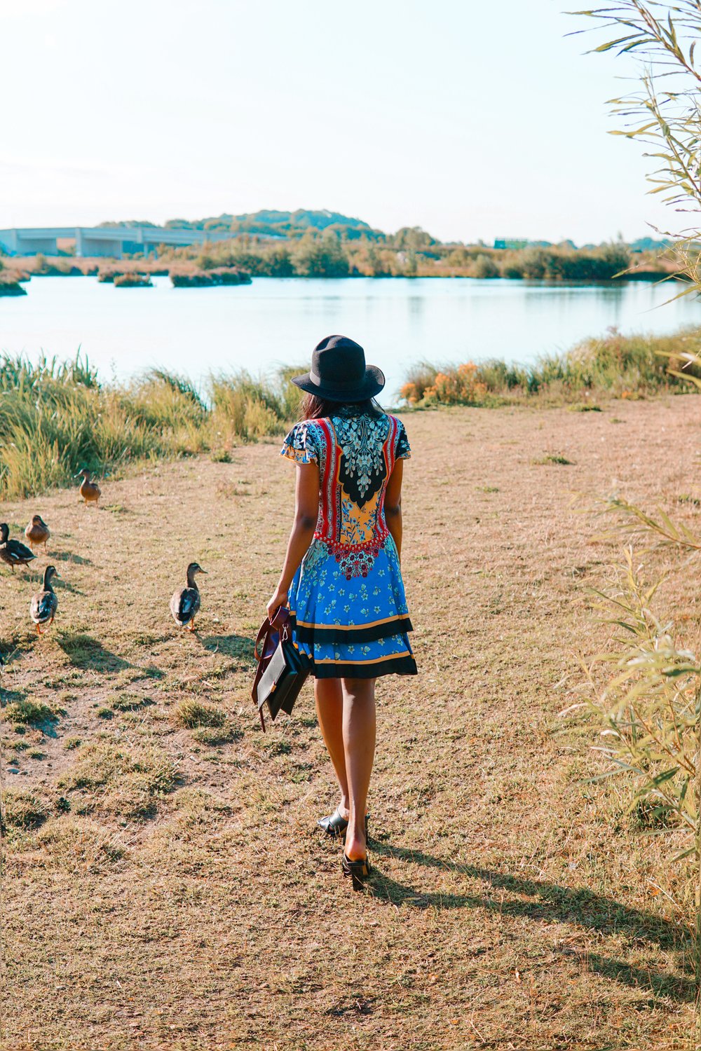 Sachini looking at a lake wearing a Alice and Olivia dress and black hat