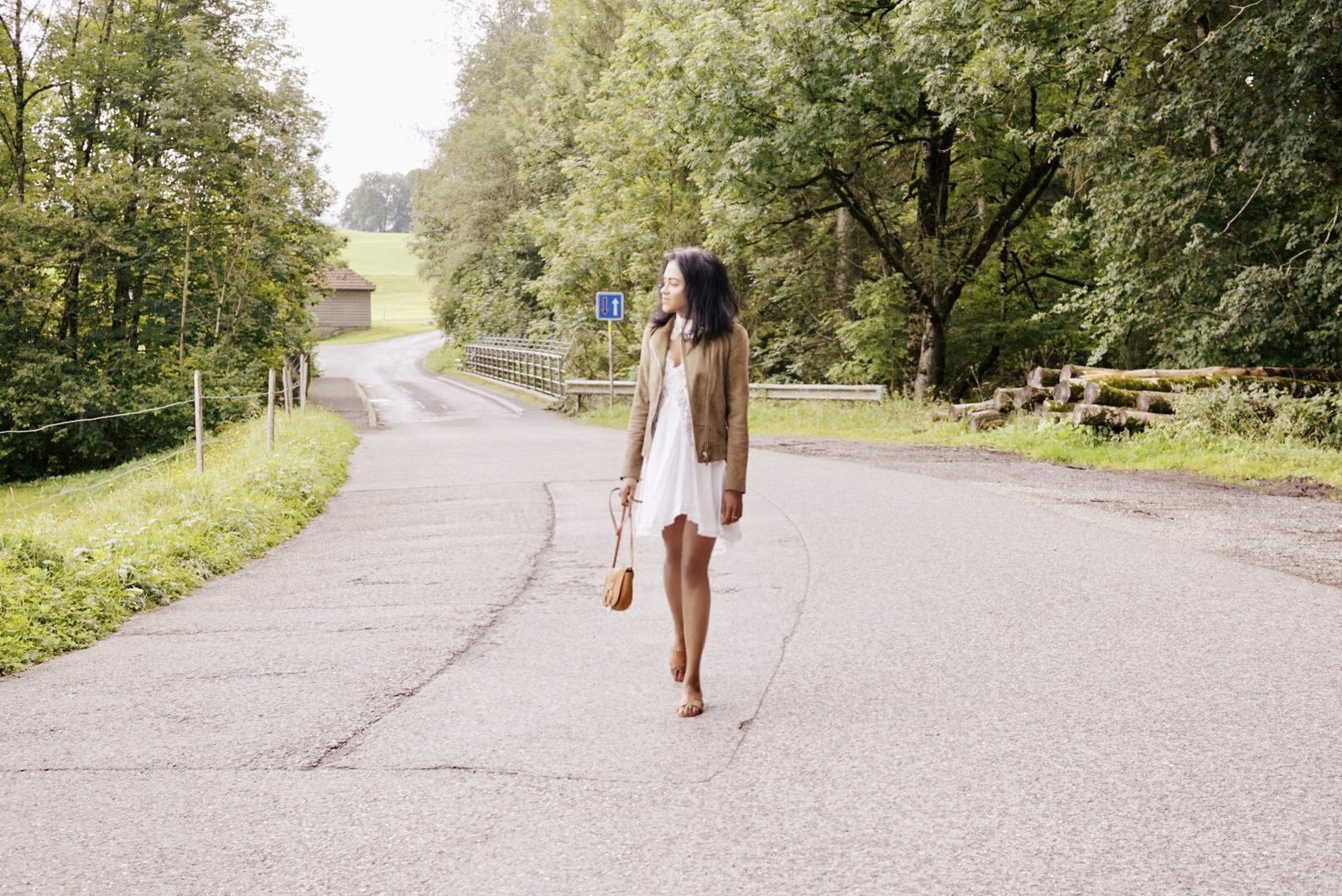 Sachini wearing a brown jacket and white dress on a country side road