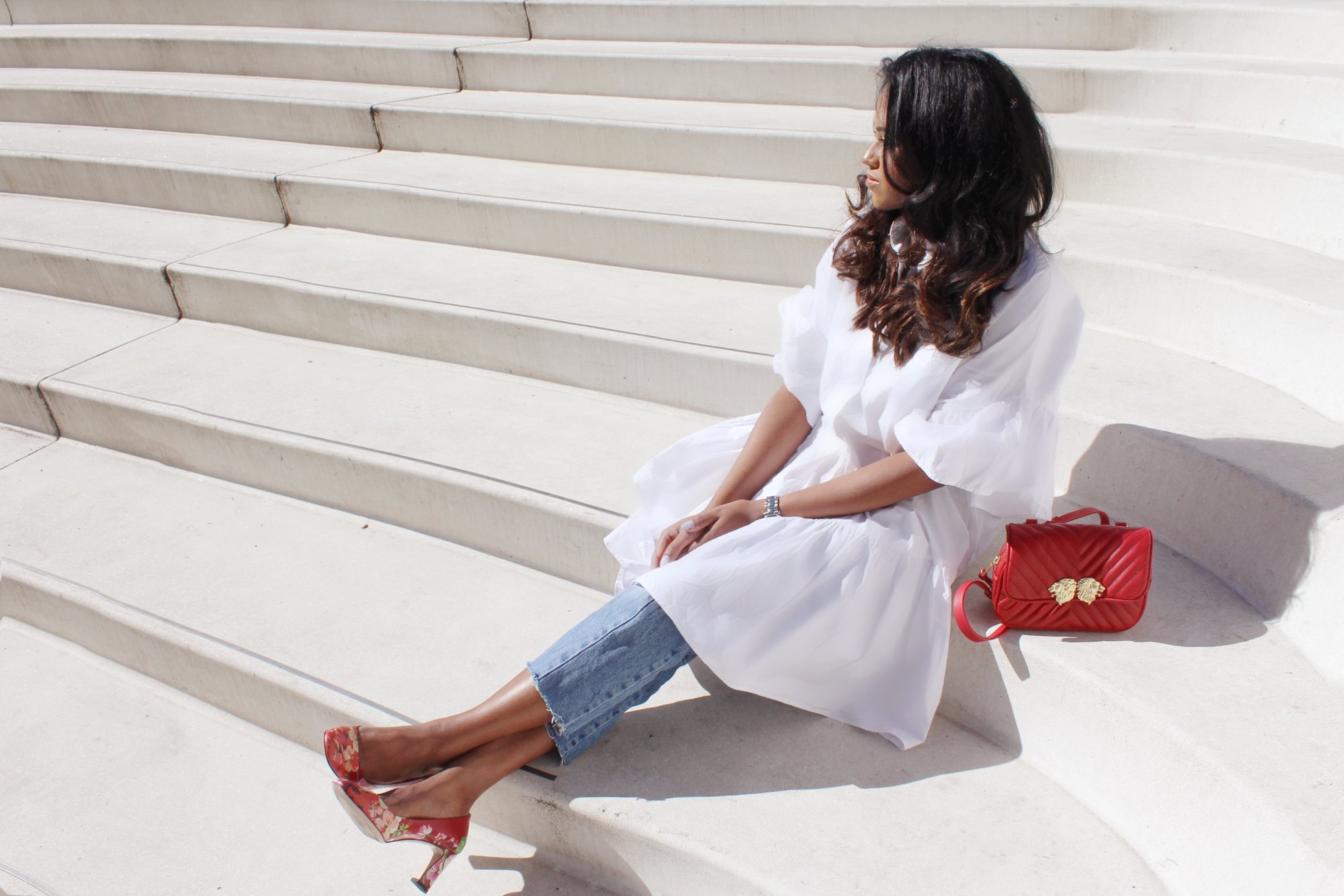 Sachini wearing a white dress, red Gucci shoes and Levi's jeans sitting a stairs