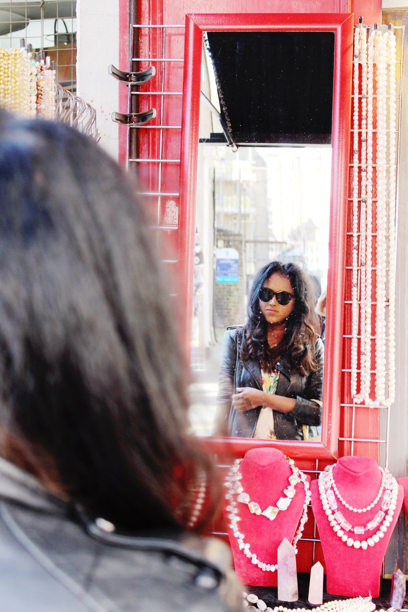Sachini wearing a black leather jacket looking in a mirror of a street shop