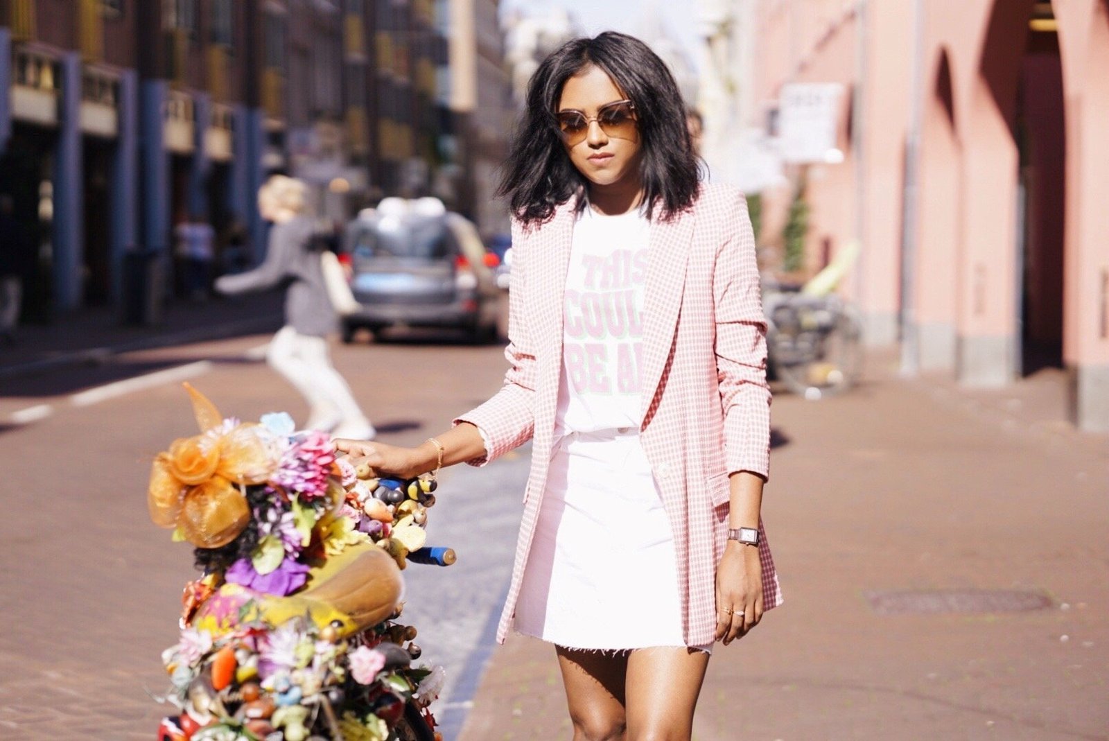 Close up of Sachini wearing a pink blazer and a white skirt in Amsterdam next to a bike decorated with flowers