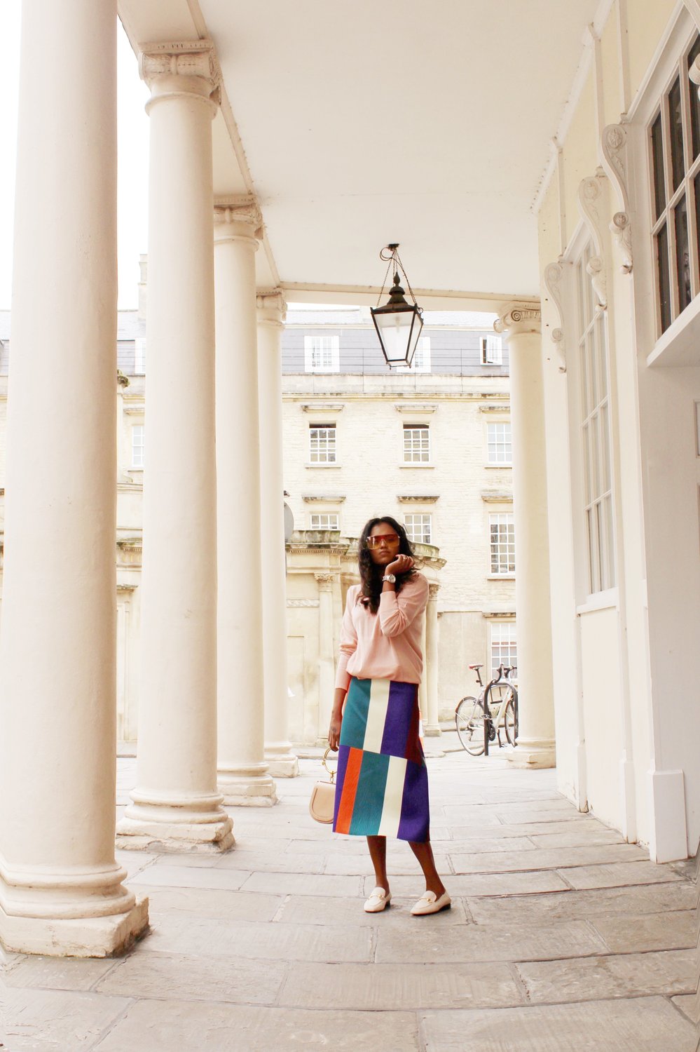 Sachini wearing sunglasses, a pink top and a colour blocked skirt holding a Chloé bag