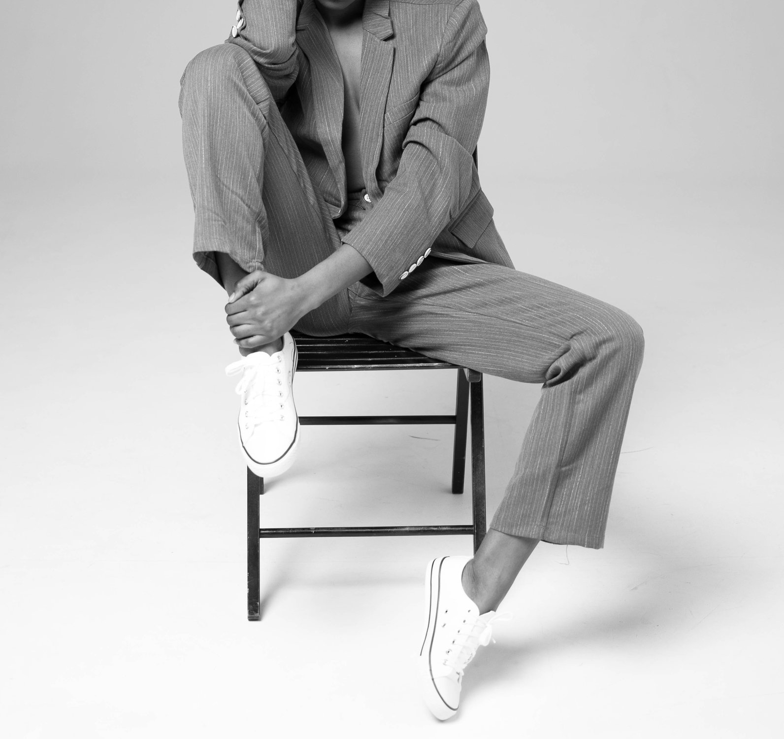 Black and white picture of model sitting on a chair with grey trousers