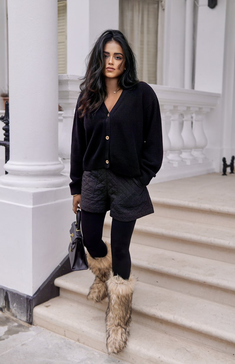 Sachini wearing a black top, shorts and leggings with faux fur boots holding a black Hermès Kelly bag