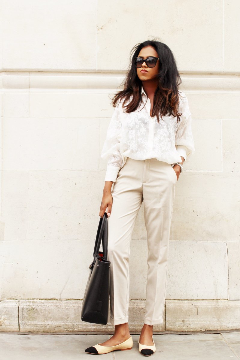 Close up of Sachini wearing a white top and beige trousers holding a black tote bag